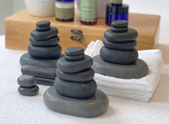 Basalt stones piled up in an artistic way on a white massage table in front of a wooden bamboo case.